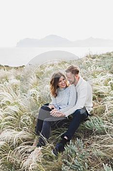 Happy young loving couple sitting in feather grass meadow, laughing and hugging