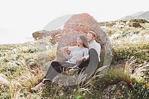 Happy young loving couple sitting in feather grass meadow, laughing and hugging