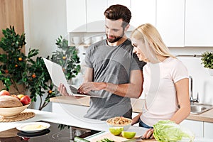 Happy young loving couple standing at kitchen and cooking