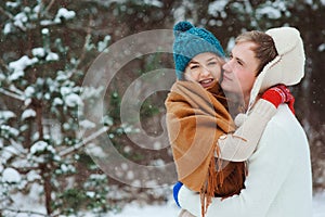 Happy young loving couple walking in snowy winter forest, covered with oversize scarf and hug.