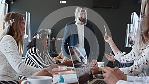 Happy young male boss leads multiethnic business people team office meeting, all wear face shields against coronavirus.