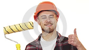 Happy young male builder holding paint roller showing thumbs up