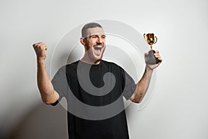 Happy young male or businessman holding his gold trophy and celebrating victory. Studio shot of man with cup as winner