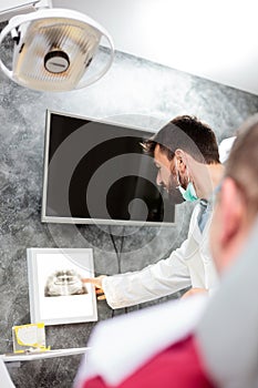 Happy young male dentist looking at patient`s x-ray images in medical clinic