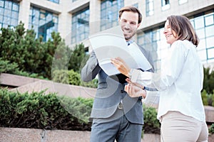 Happy young male and female business people talking in front of an office building, having a meeting and discussing