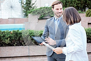 Happy young male and female business people talking in front of an office building, having a meeting and discussing