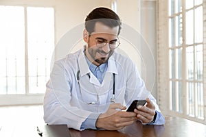 Happy young male gp doctor using cellphone applications.