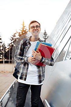 Happy young male student in casual outfit with bright smile holding folders while standing on the street