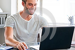 Happy young male student smiling while seated behind his laptop