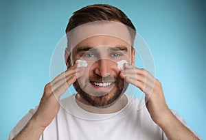 Happy young man applying facial cream on blue background