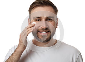 Happy young man applying facial cream on white background
