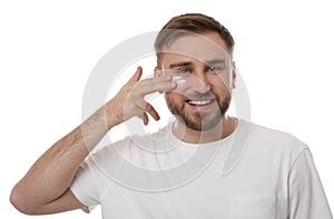 Happy young man applying facial cream on white background