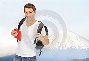 Happy young man with backpack and book travelling