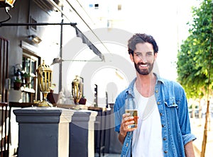 Happy young man in blue shirt holding glass of beer outdoors