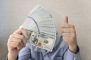 Happy young man in blue t-shirt holding money and showing thumbs up on white background. getting a salary, big cashback