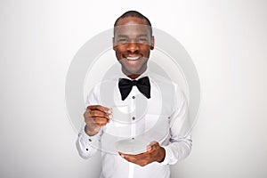 Happy young man in bowtie holding cup of coffee against white background