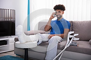 Happy Young Man With Broken Leg Talking On Mobile Phone
