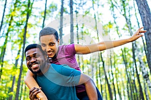 Happy young man carrying his beautiful woman on his back at the forest