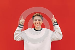 Happy young man in casual clothes looks at the camera with a smile on his face and shows thumbs up on copy space