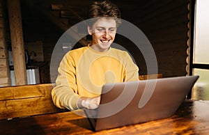 Happy young man in casual clothes sitting at a wooden table in the country and working on a laptop. Work on the Internet with a