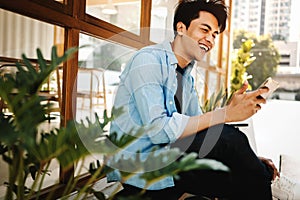 Happy Young Man in Casual wear Using Mobile Phone while Sitting in front of the Cafe