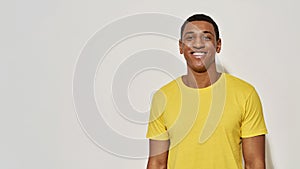 Happy young man in casual yellow t shirt smiling at camera while posing isolated over gray background