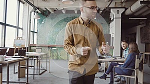 Happy young man in cheerful mood walking through the office and dancing crazy. Businessman greets with colleagues.