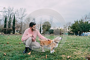 Happy young man crouched petting his dog walking in park