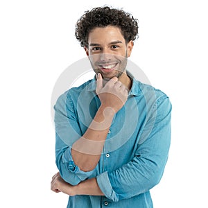 happy young man with curly hair holding hand to chin and thinking