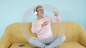 Happy young man dancing while listening to music with headphones sitting on sofa