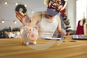 Happy young man decides to start saving up in the new year and puts money in smiley piggy bank