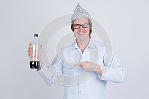 Happy young man doctor with tinfoil hat holding and pointing at bottle of soda