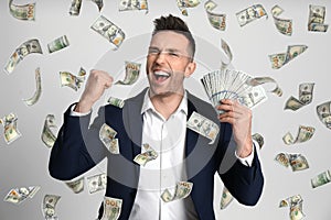 Happy young man with dollars under money rain on background