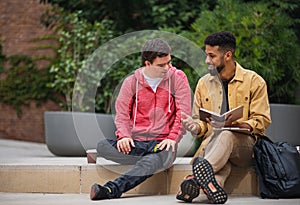 Happy young man with Down syndrome and mentoring friend sitting and talking outdoors