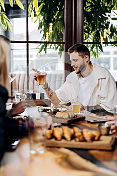 Happy young man drinking draft beer while having fun in pub or bar with friends and laughing