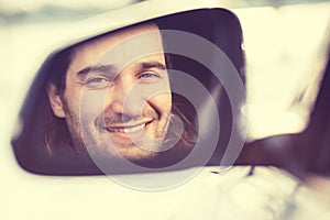 Happy young man driver looking in car side view mirror