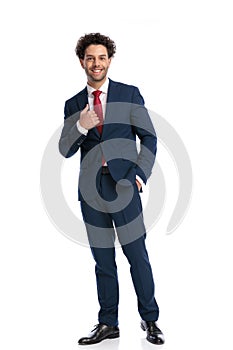 Happy young man in elegant suit smiling, holding hand in pocket and fixing suit