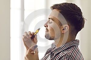 Happy young man enjoying aromatherapy and smelling essential oil from roller bottle