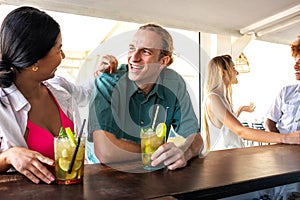 Happy young man enjoying mojito cocktail with girlfriend at a beach bar drinking. Young multiracial couple on a date.