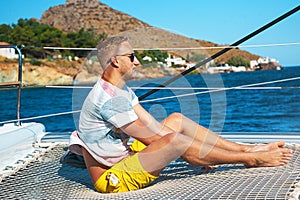 Happy young man feels happy on the luxury sail boat yacht catamaran in turquoise sea in summer holidays on island.