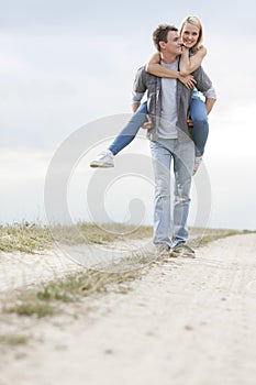 Happy young man giving piggyback ride to woman on trail at field