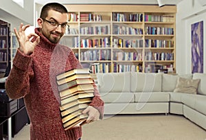 Happy young man in glasses with the books at library