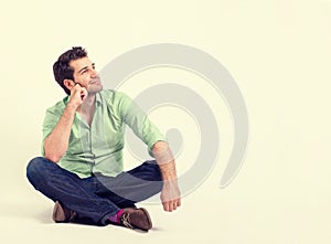 Happy young man in green shirt and blue jeans sitting on the floor