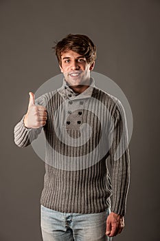 Happy young man in grey sweater showing thumb up