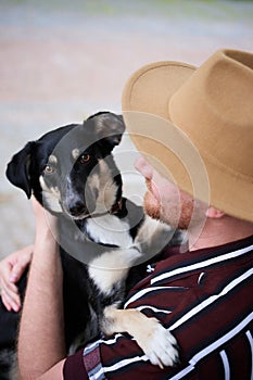 Happy young man in hat hugging his rescued dog looking at the camera outdoors