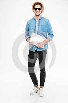 Happy young man in hat and sunglasses holding laptop