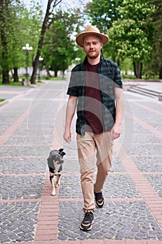 Happy young man in hat walking his rescued dog looking at the camera outdoors