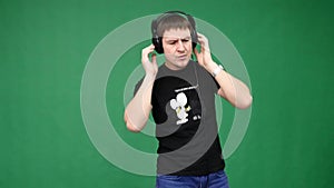 Happy young man in headphones dancing and listen music on green background