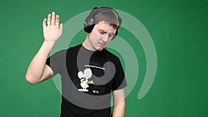 Happy young man in headphones dancing and listen music on green background