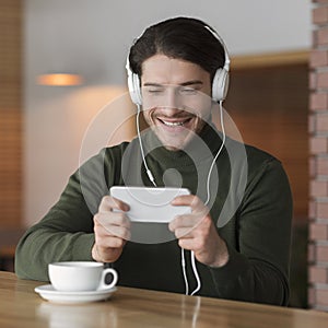 Happy young man in headset using mobile phone at cafe